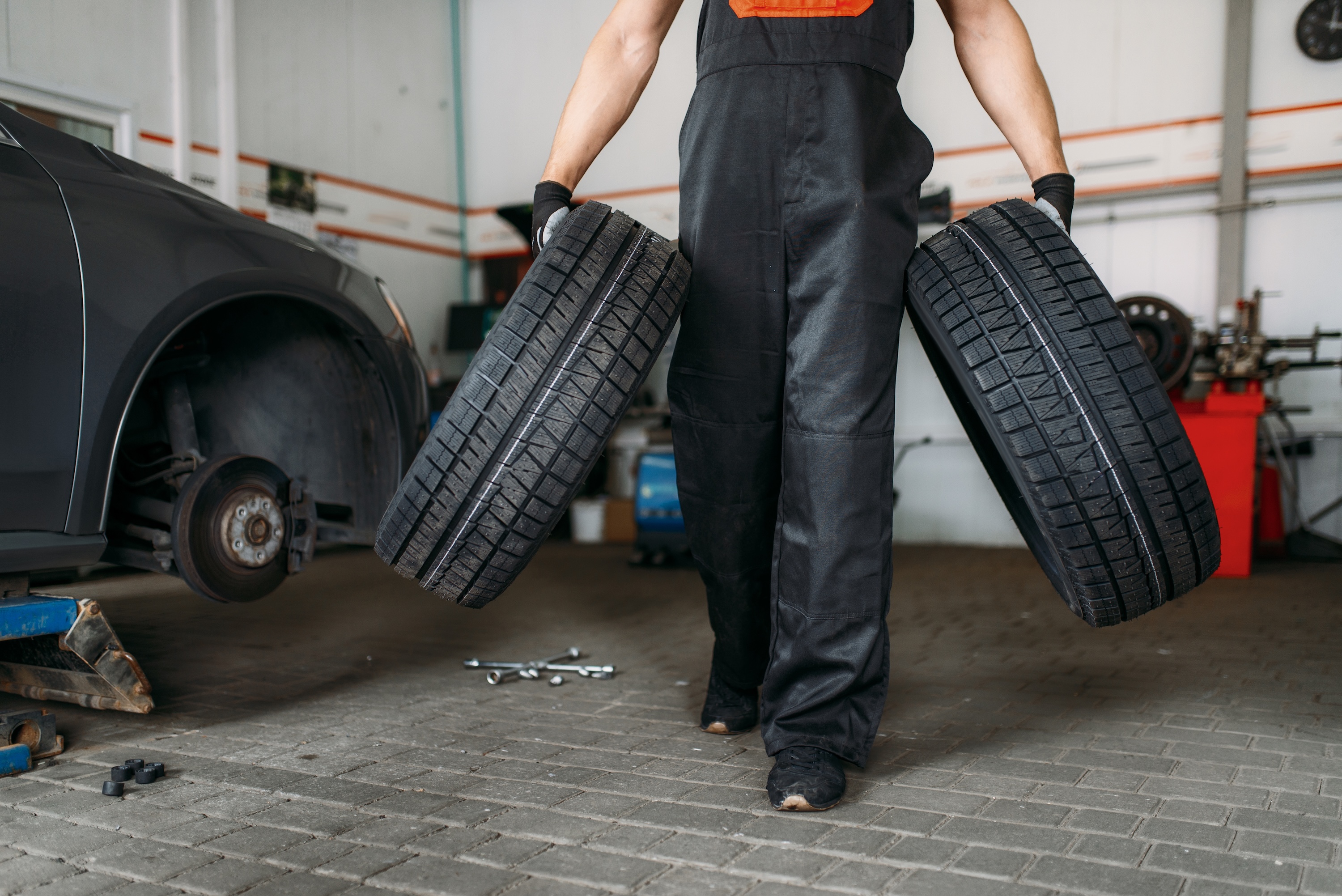 Mechanic carrying two car tyres across the workshop